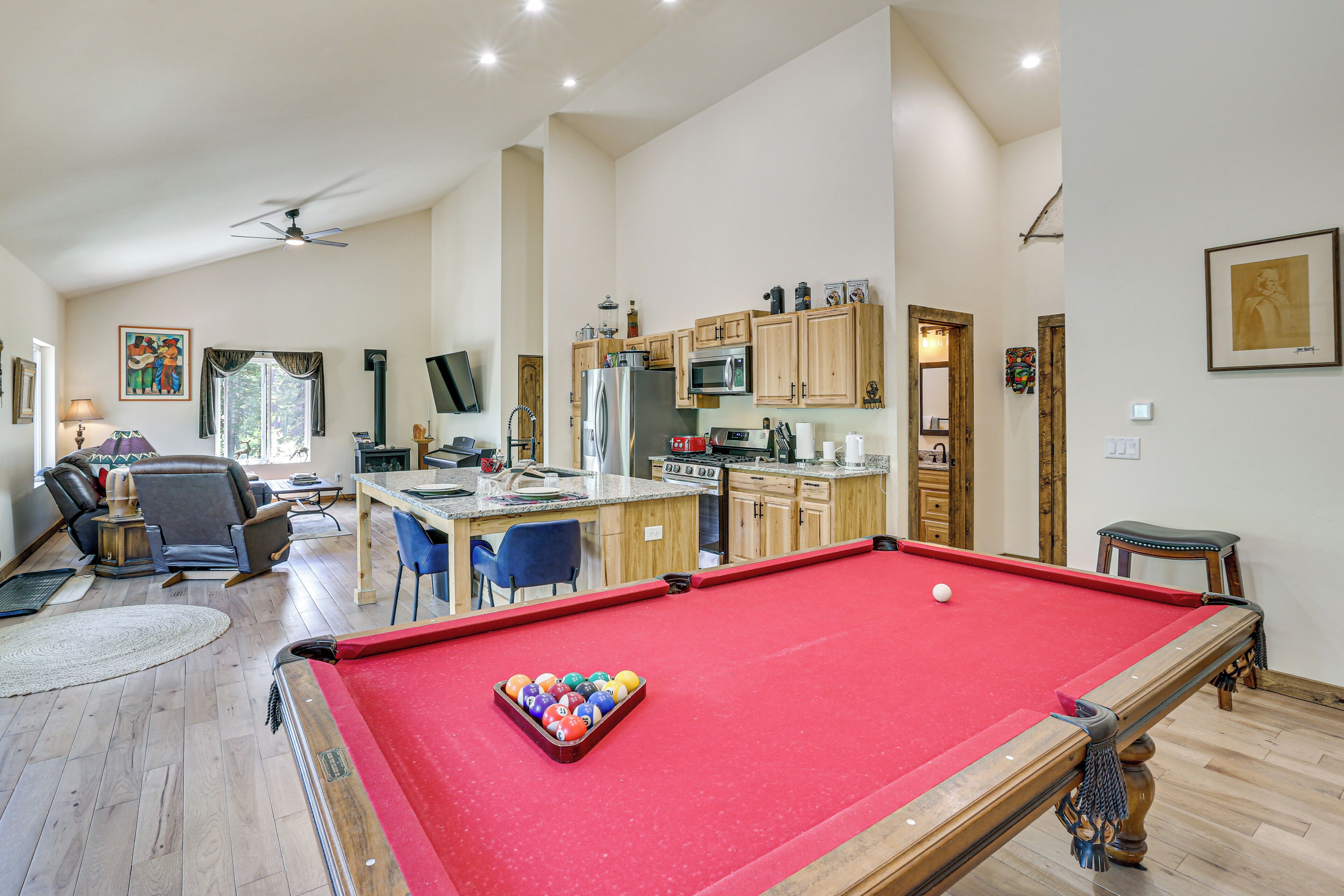 A spacious living area with a pool table, a kitchen with wooden cabinets, and a dining area with blue chairs.