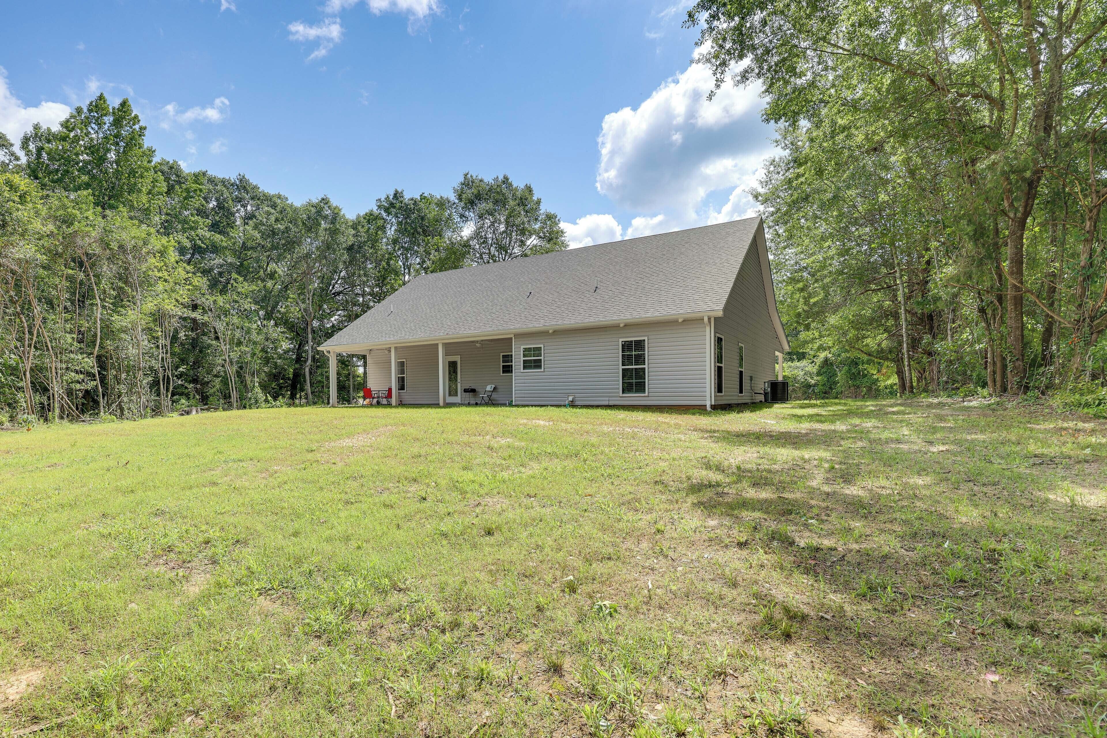 A single-story house with a covered porch, surrounded by a grassy yard and trees.
