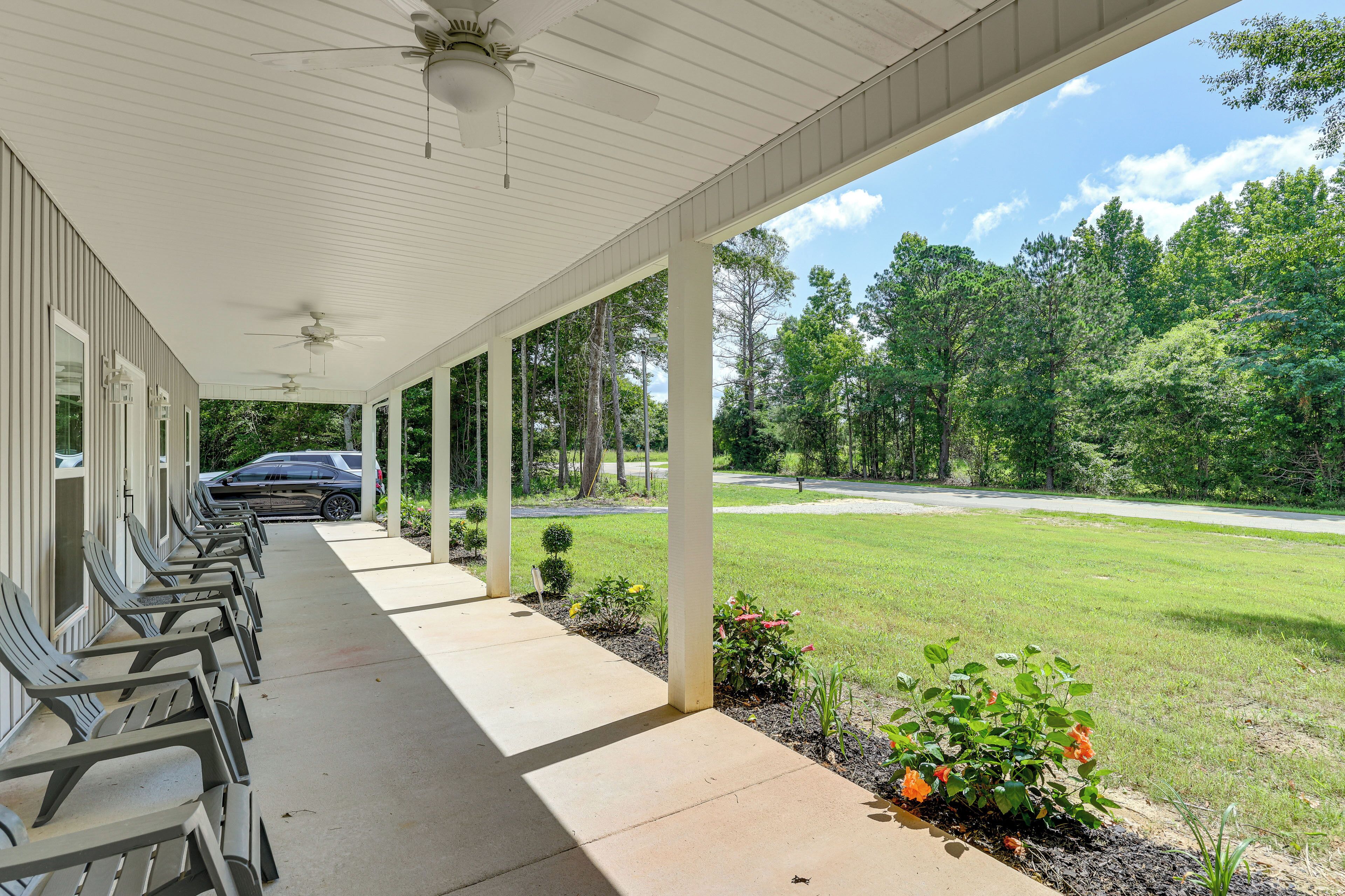A covered outdoor area with rows of chairs, a lawn, and trees in the background.