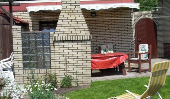 A brick building with a red table and chairs outside, a wooden door, and a window with a decorative grille.