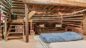 A rustic log cabin interior with a loft bed, a brown sofa, and a cozy fireplace. - 12 Mi to Staunton River State Park: Off-grid Cabin (Scottsburg)