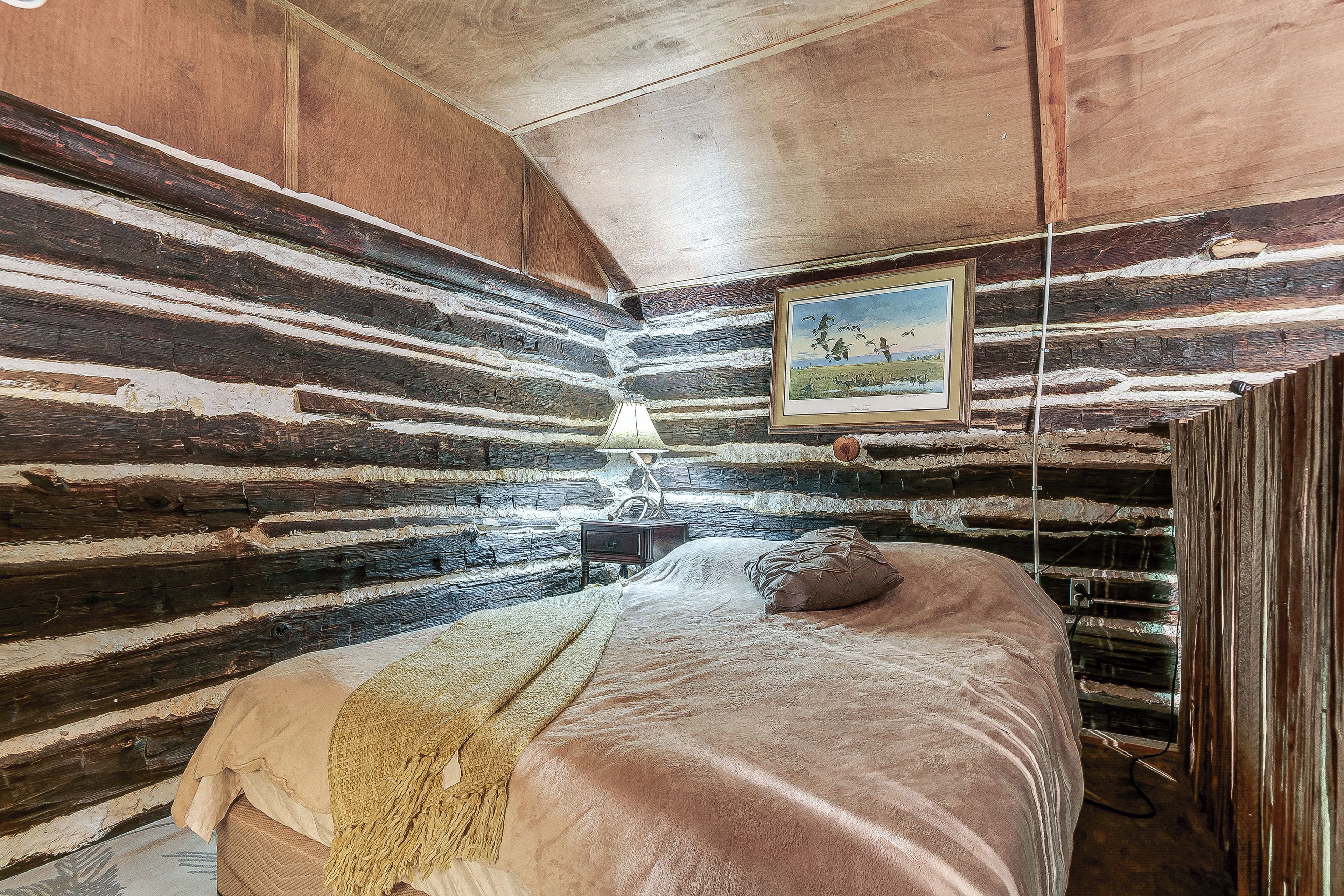 A log cabin room with a bed, a lamp, and a framed picture on the wall.