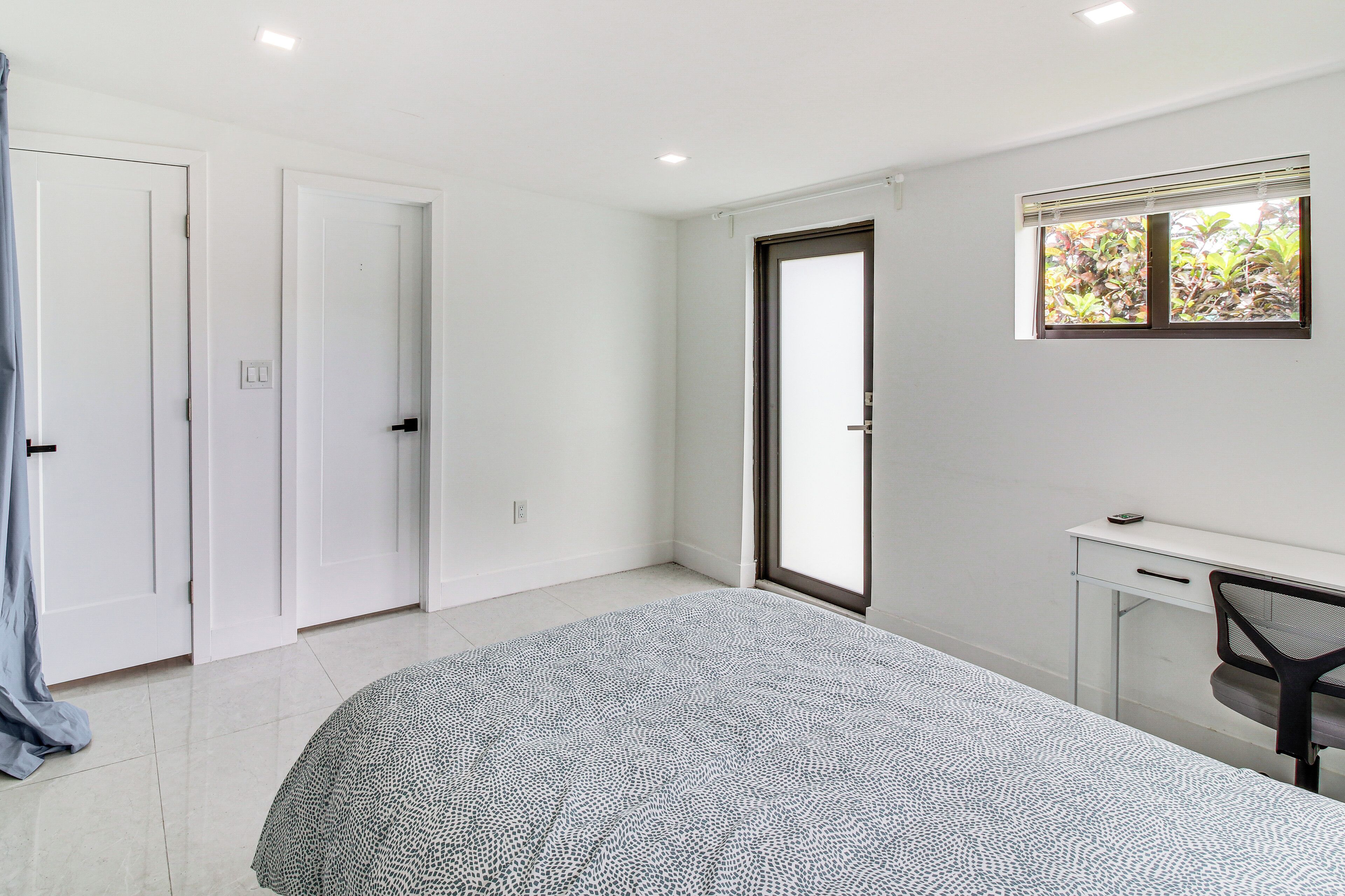 A bedroom with a bed, a desk, a chair, and a window.