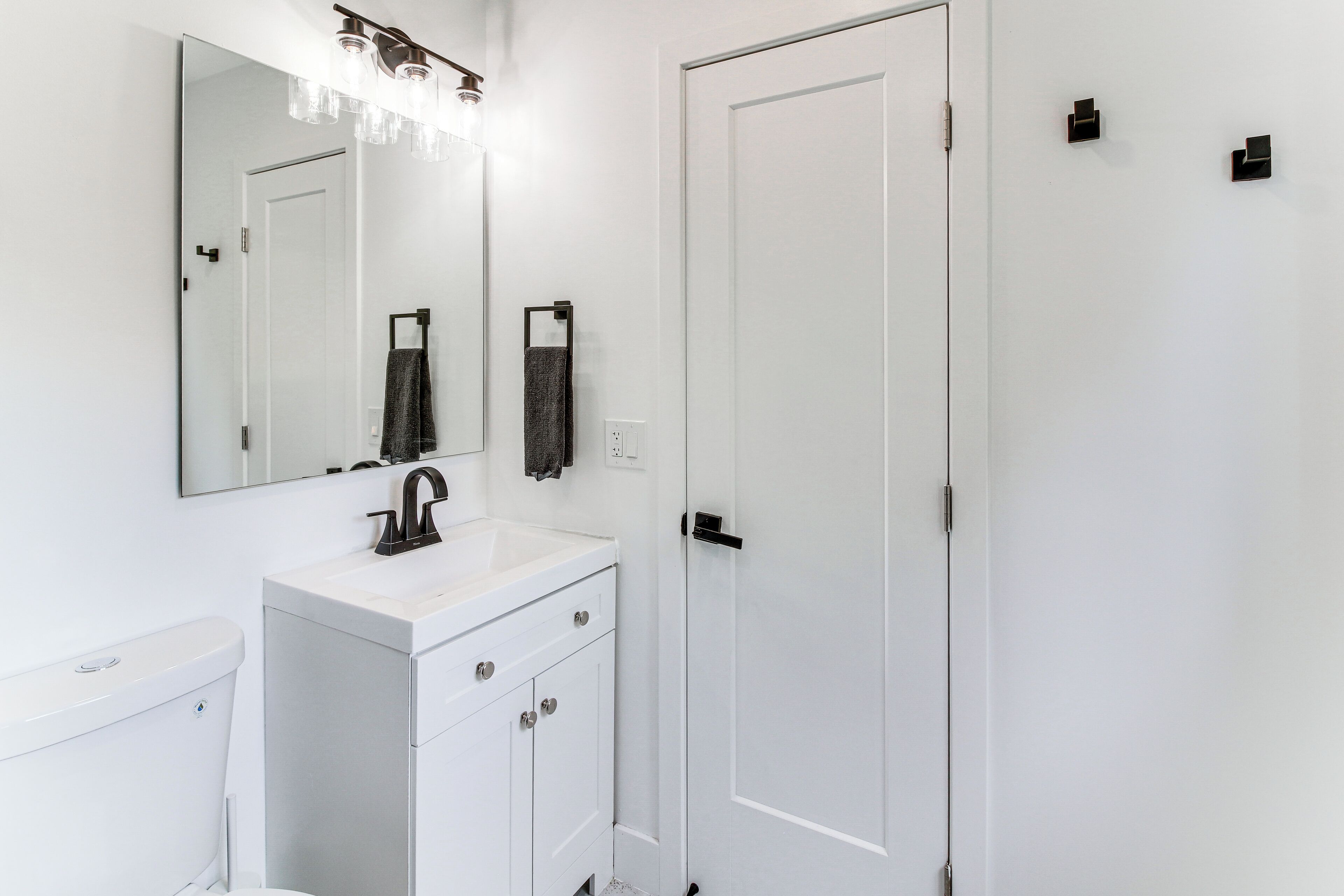 Une salle de bain moderne avec un meuble-lavabo blanc, un grand miroir et une porte blanche.