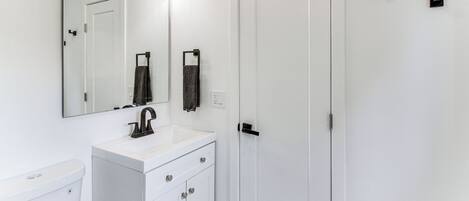 Une salle de bain moderne avec un meuble-lavabo blanc, un grand miroir et une porte blanche.