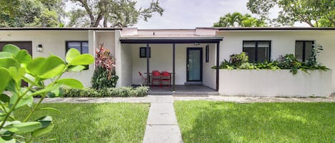 A modern house with a covered patio, a lawn, and a pathway leading to the entrance.