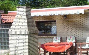 A brick building with a tiled roof, a window, and a table with chairs.