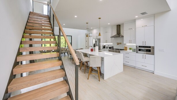 A modern kitchen with white cabinets, a central island, and a staircase with wooden steps. - Walk to Celebration Park: Naples Home w/ Pool! (Naples)