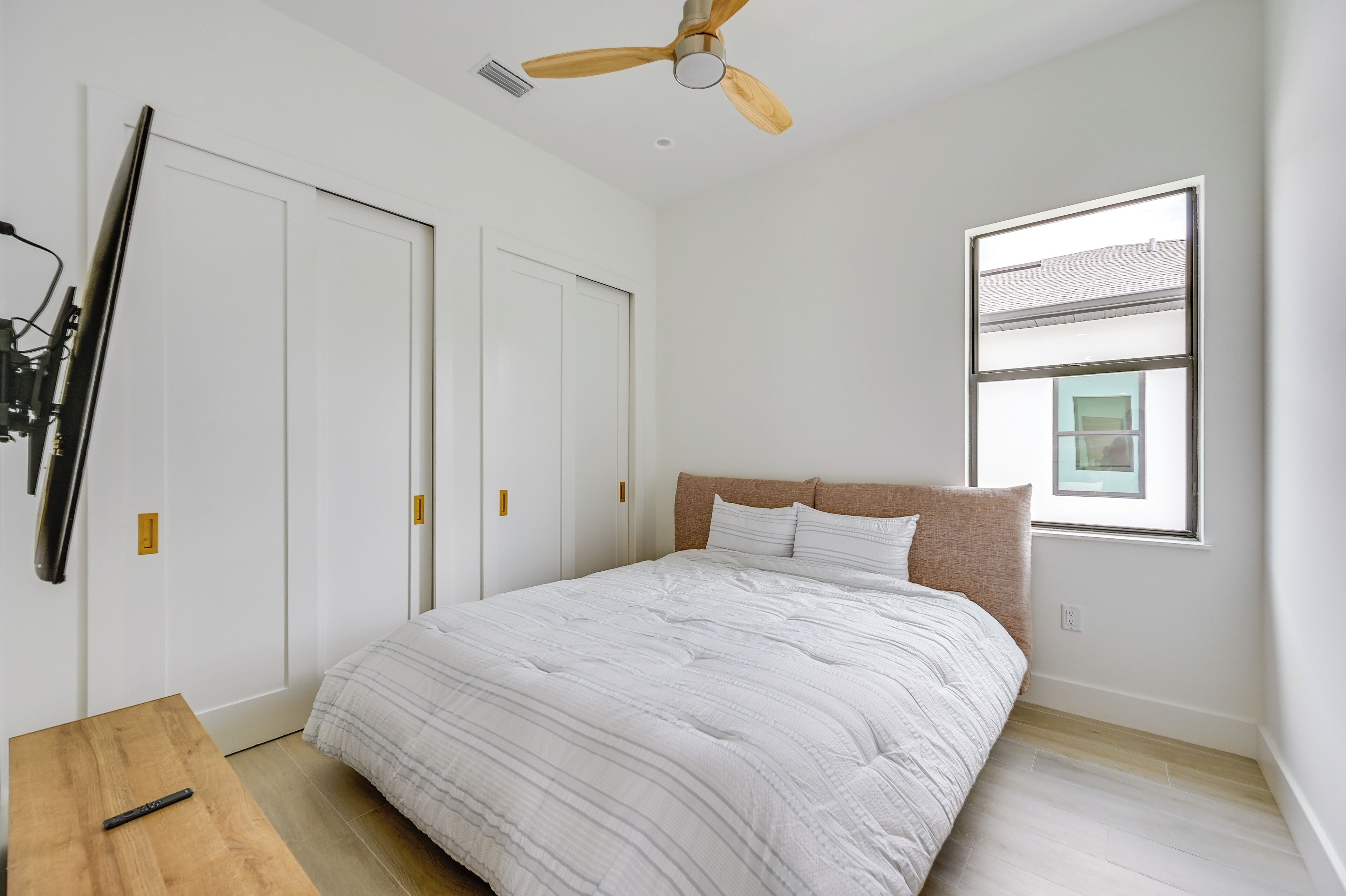 A bedroom with a bed, a ceiling fan, a window, and a door.