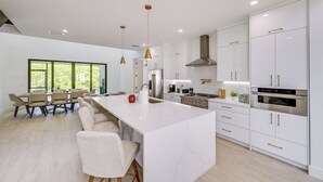 A modern kitchen with white cabinetry, a large island, and pendant lighting. - Walk to Celebration Park: Naples Home w/ Pool! (Naples)