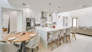 A modern kitchen with white cabinetry, a central island, and a dining area with a round table and chairs. - Walk to Celebration Park: Naples Home w/ Pool! (Naples)