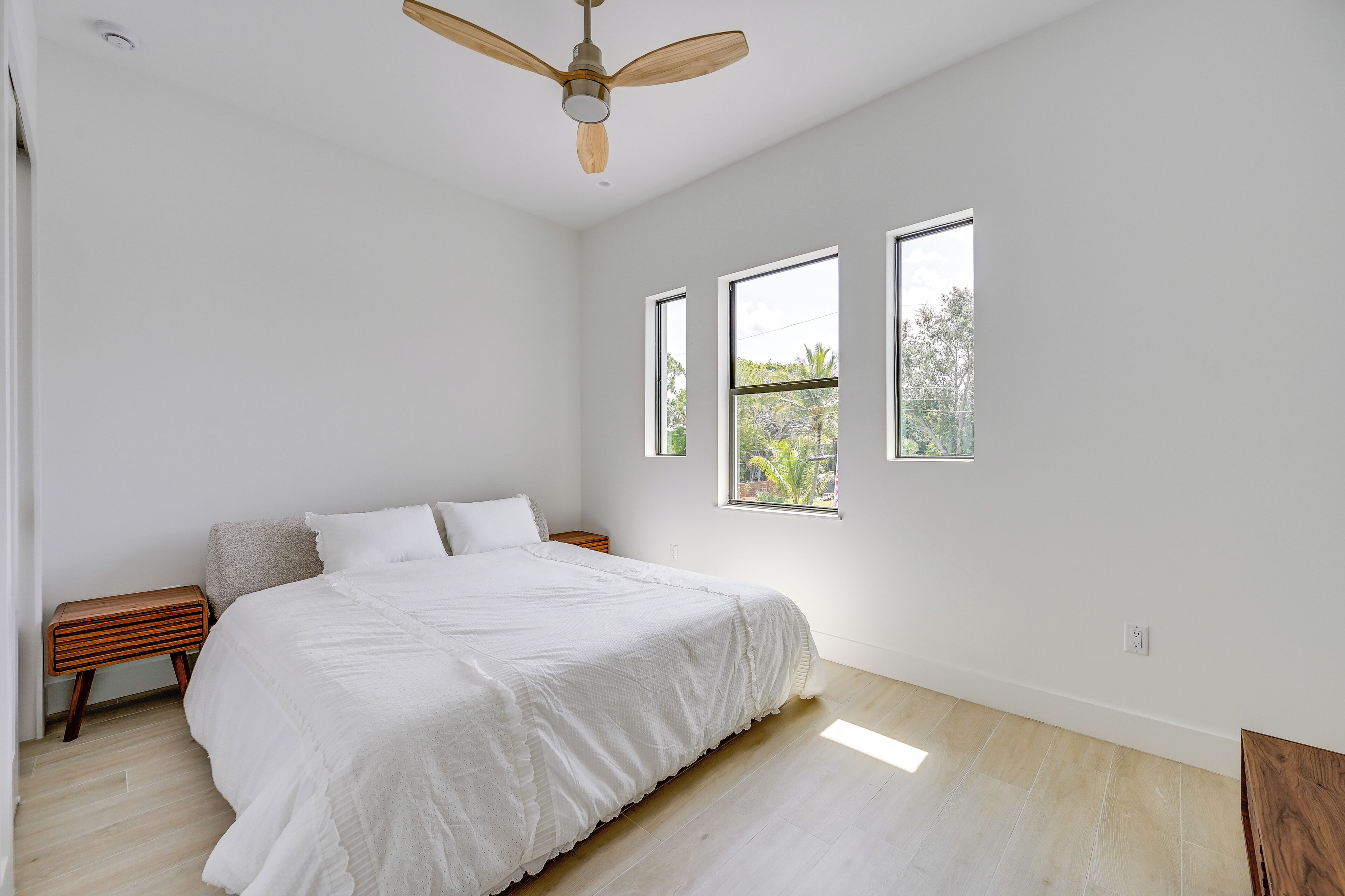 Una camera da letto con un letto, comodini in legno, una ventola a soffitto e tre finestre.