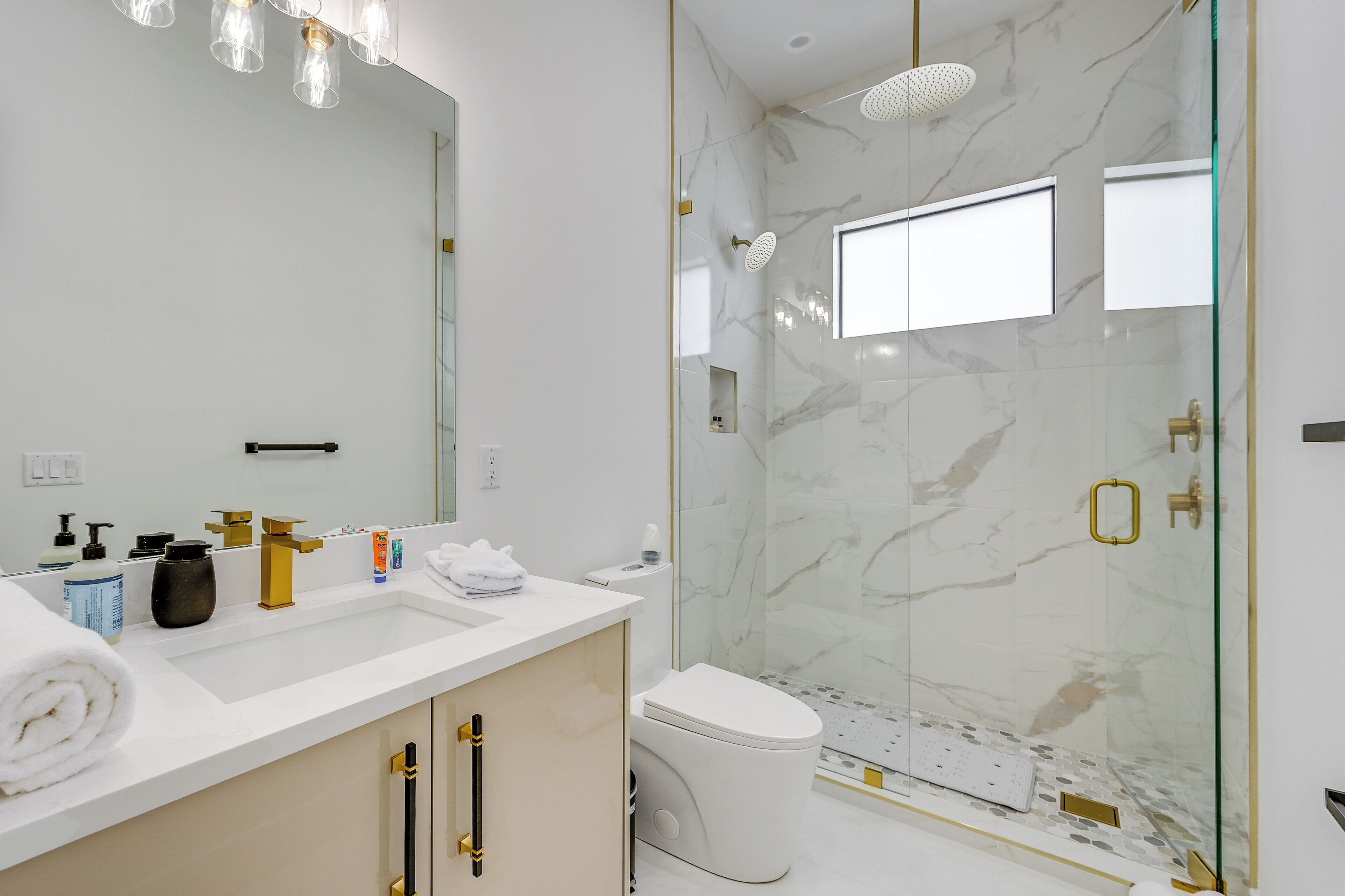 A modern bathroom with a white sink, gold fixtures, a glass-enclosed shower, and a marble backsplash.