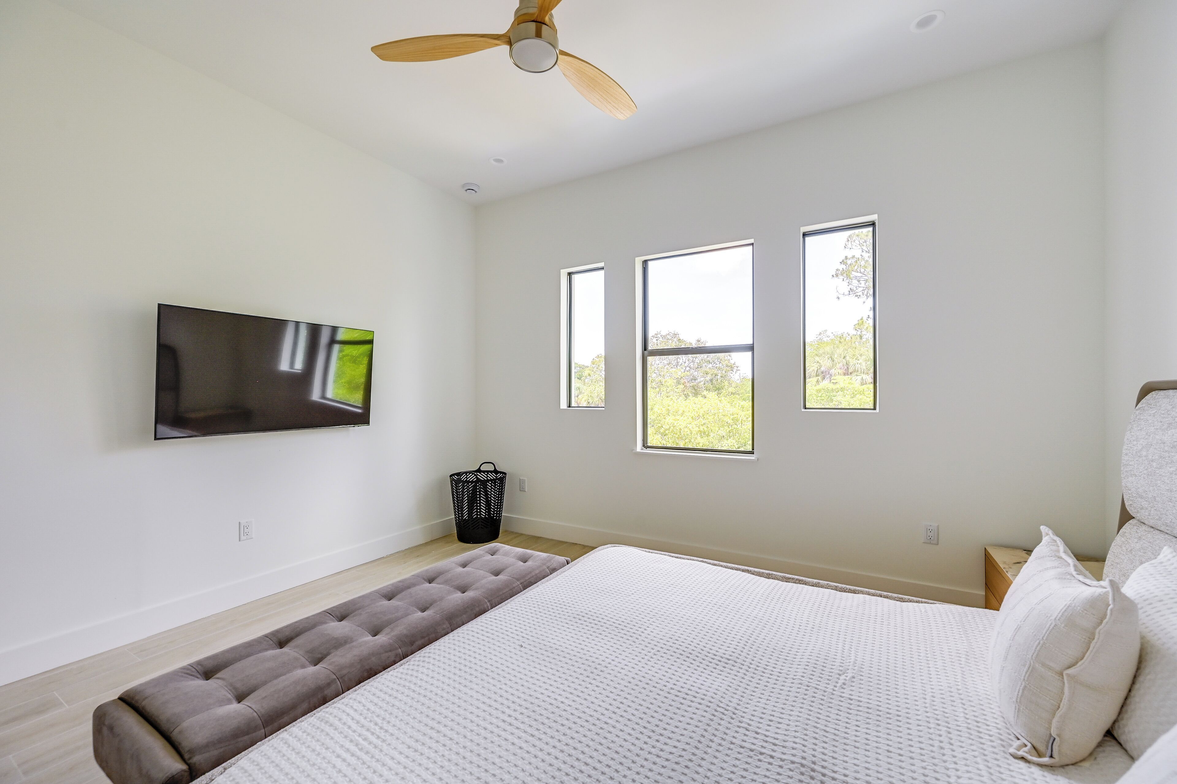 Une chambre à coucher avec un lit, un ventilateur de plafond, une télévision et trois fenêtres.