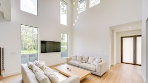 Een ruime woonkamer met een grote flatscreen-tv, twee banken, een salontafel en grote ramen met uitzicht op groen.