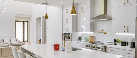 Cocina moderna con armarios blancos, una isla central y tiradores dorados.