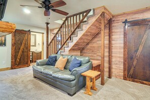 Un salon avec un canapé en cuir, un escalier en bois et un ventilateur de plafond.