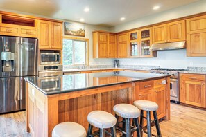 Une cuisine moderne avec des meubles en bois, des appareils électroménagers en acier inoxydable et un grand îlot central doté de tabourets.