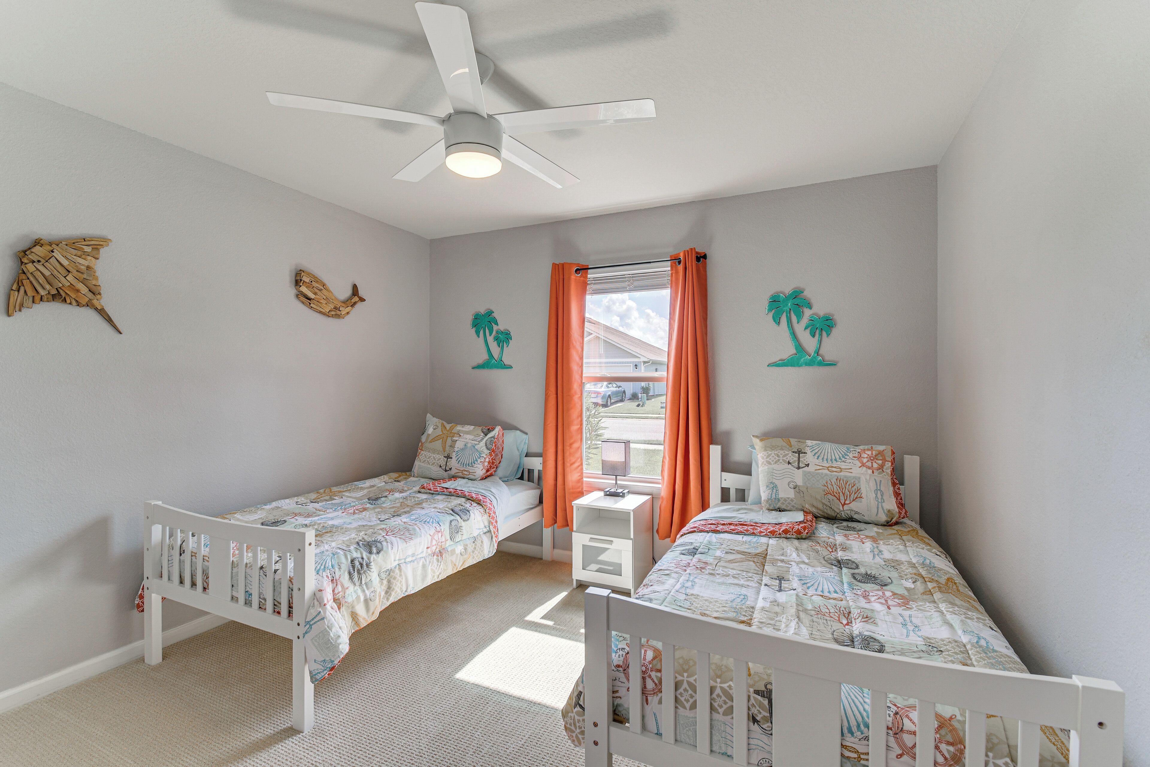 Une chambre avec deux lits simples, un ventilateur de plafond et une fenêtre avec des rideaux orange.