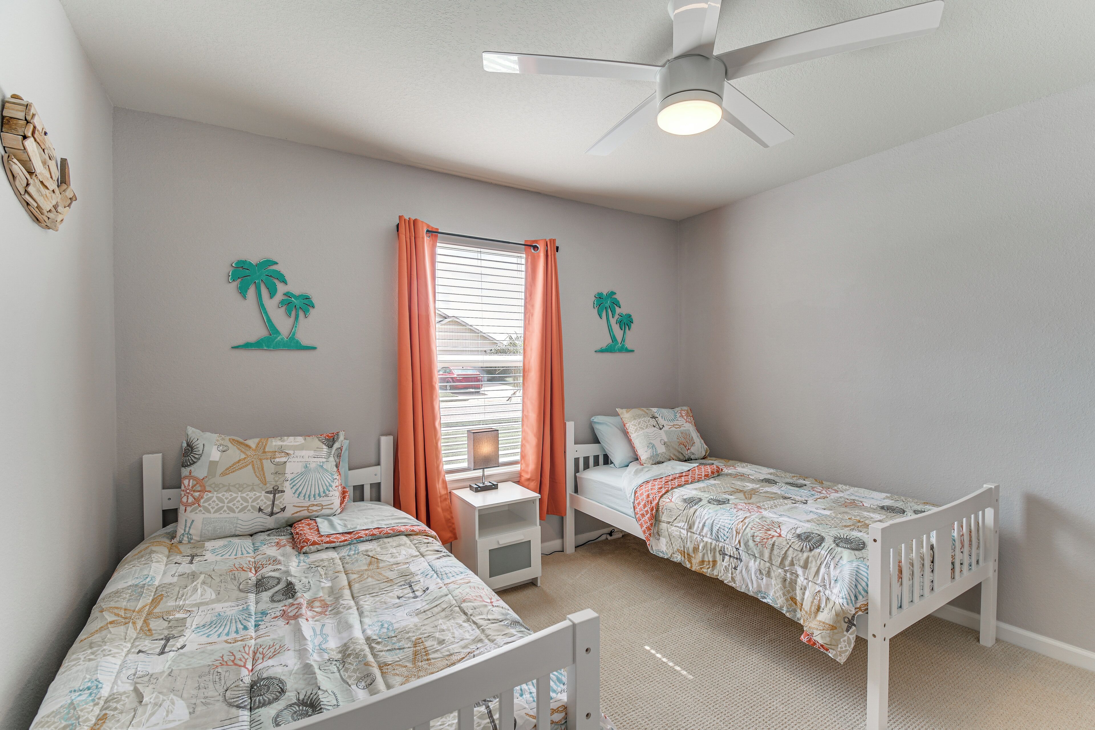 A bedroom with two single beds, a ceiling fan, a window with curtains, and wall decorations.