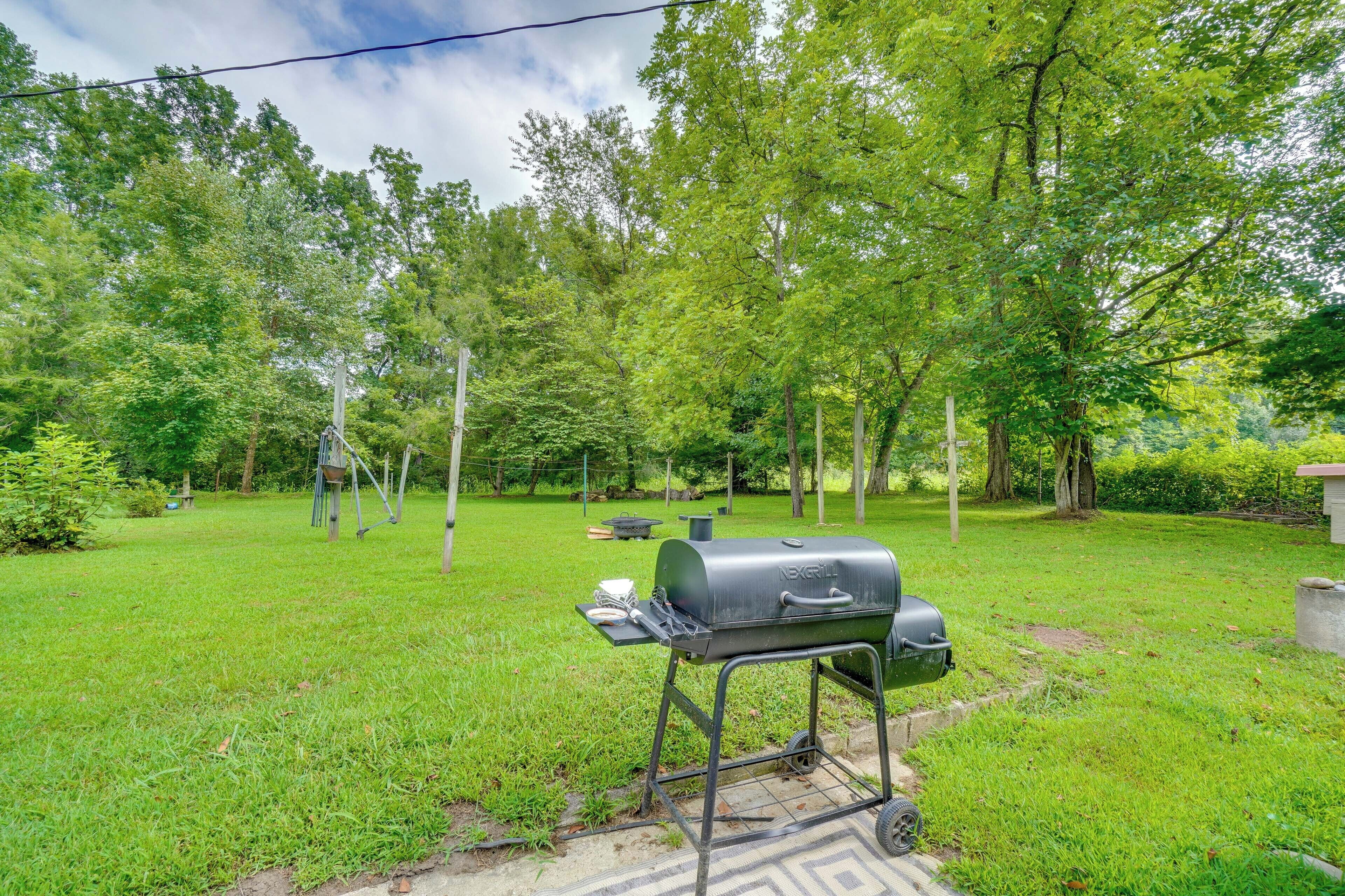 Un patio trasero con una parrilla portátil, una mesa de picnic y un césped bien cuidado.