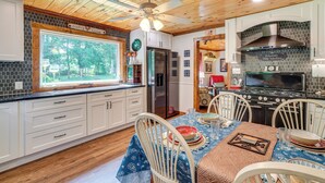 A kitchen with wooden ceiling, white cabinets, a dining table with chairs, and a stove. - Riverfront Cabin - 6 Mi to Great Smoky Mtns NP! (Townsend)