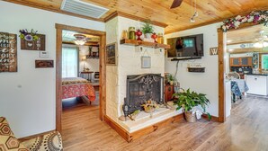 A cozy living room with a fireplace, wooden ceiling, and a TV mounted on the wall. - Riverfront Cabin - 6 Mi to Great Smoky Mtns NP! (Townsend)