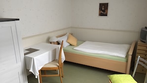 A small, neatly arranged room with a bed, a desk, a chair, and a television.