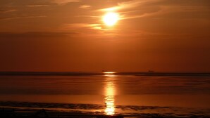 A sunset over a calm body of water with a distant ship and a person standing on the shore.
