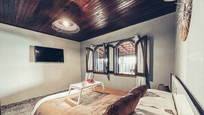 A bedroom with a bed, a bedside table, a TV, and a window with curtains.