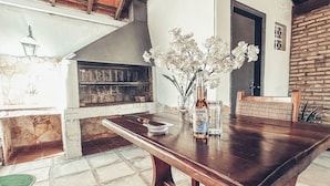 A wooden table with a Corona beer bottle and a glass, a vase with white flowers, and a stone fireplace in a rustic room.