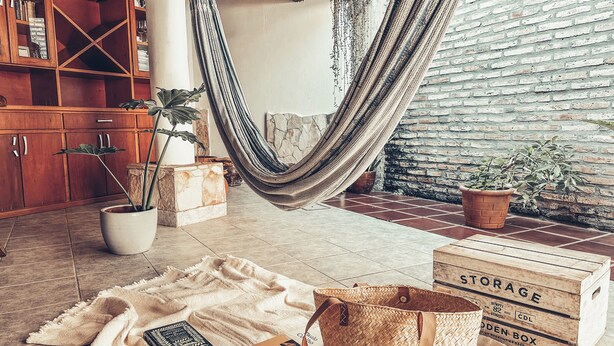 A cozy room with a hammock, wooden furniture, and potted plants.