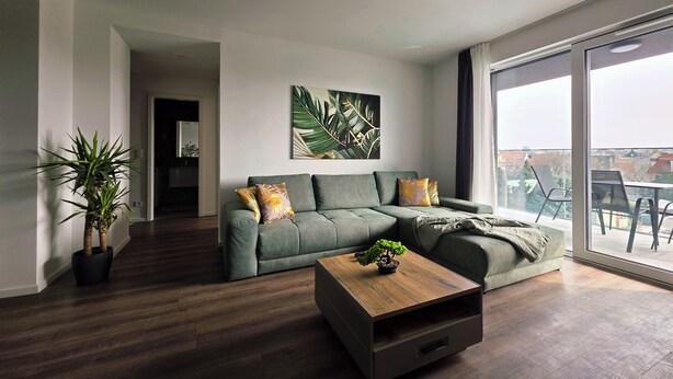 Una sala de estar moderna con un sofá verde, una mesa de centro de madera y un ventanal con vistas a la ciudad.