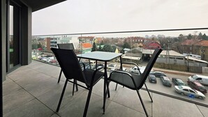 Un balcón con mesa y sillas, con vista a un estacionamiento y edificios.