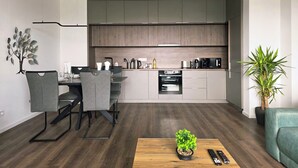 Una cocina moderna con gabinetes grises, un comedor con sillas grises, una mesa de centro de madera con una planta y un sofá verde.