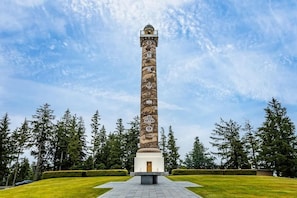 Un monument haut et cylindrique, orné de sculptures complexes, entouré d’une pelouse bien entretenue et de grands arbres.