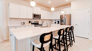 A modern kitchen with white cabinetry, a central island with bar stools, stainless steel appliances, and pendant lighting. - 15807 Luxury 8 Bedroom Family Home With Game Room (Clermont)
