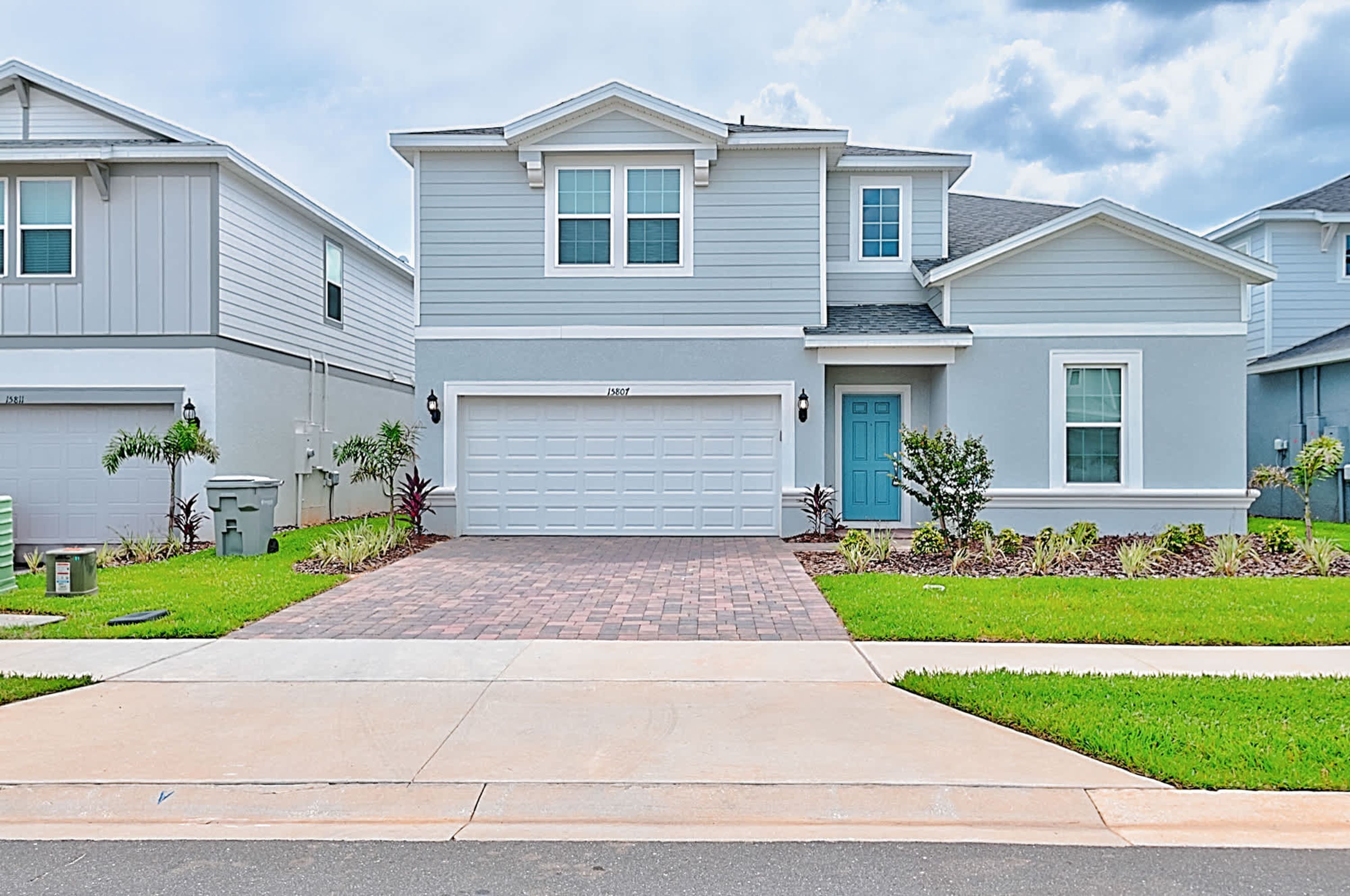 A two-story residential building with a garage, a front door, and a small front yard with plants.
