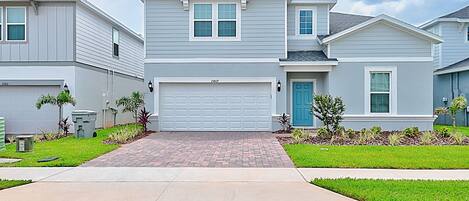 A two-story residential building with a garage, a front door, and a small front yard with plants.