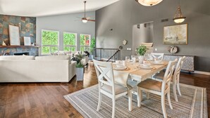 A modern dining area with a wooden table set for four, white chairs, and a chandelier.