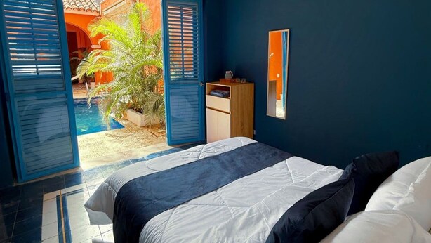A bedroom with a bed, a ceiling fan, a view of a courtyard, and a door leading outside. - Nok Charming Colonial Villa Ctg (Cartagena)