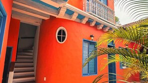 A brightly colored building with a staircase leading to a balcony, surrounded by palm trees. - Nok Charming Colonial Villa Ctg (Cartagena)