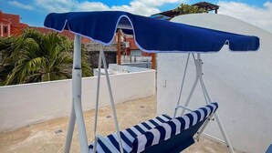 A blue and white striped lounge chair with a canopy, set on a rooftop terrace with a clear blue sky and distant buildings. - Nok Charming Colonial Villa Ctg (Cartagena)