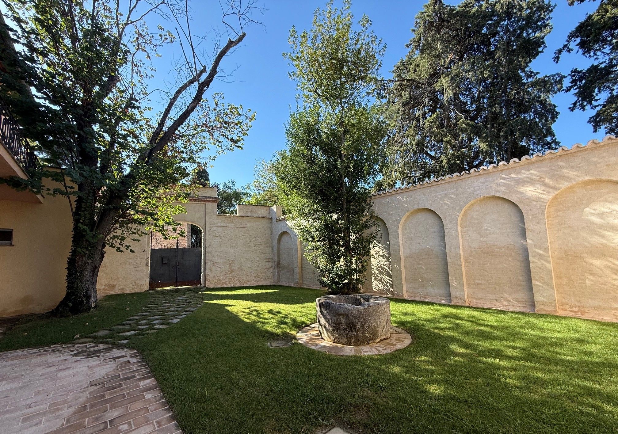 Une cour avec un chemin pavé, un petit arbre et un mur agrémenté de fenêtres en arc de cercle.