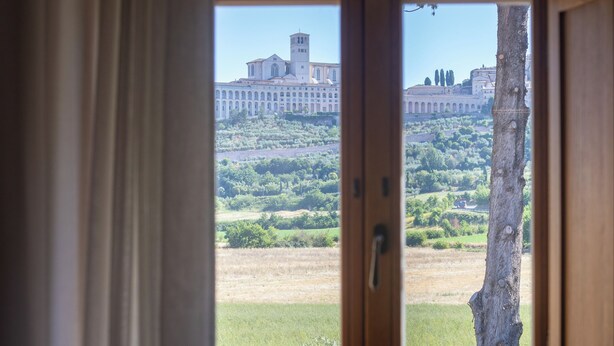 A room with a large window overlooking a historic building and a tree. - Ascesi Resort (Assisi)