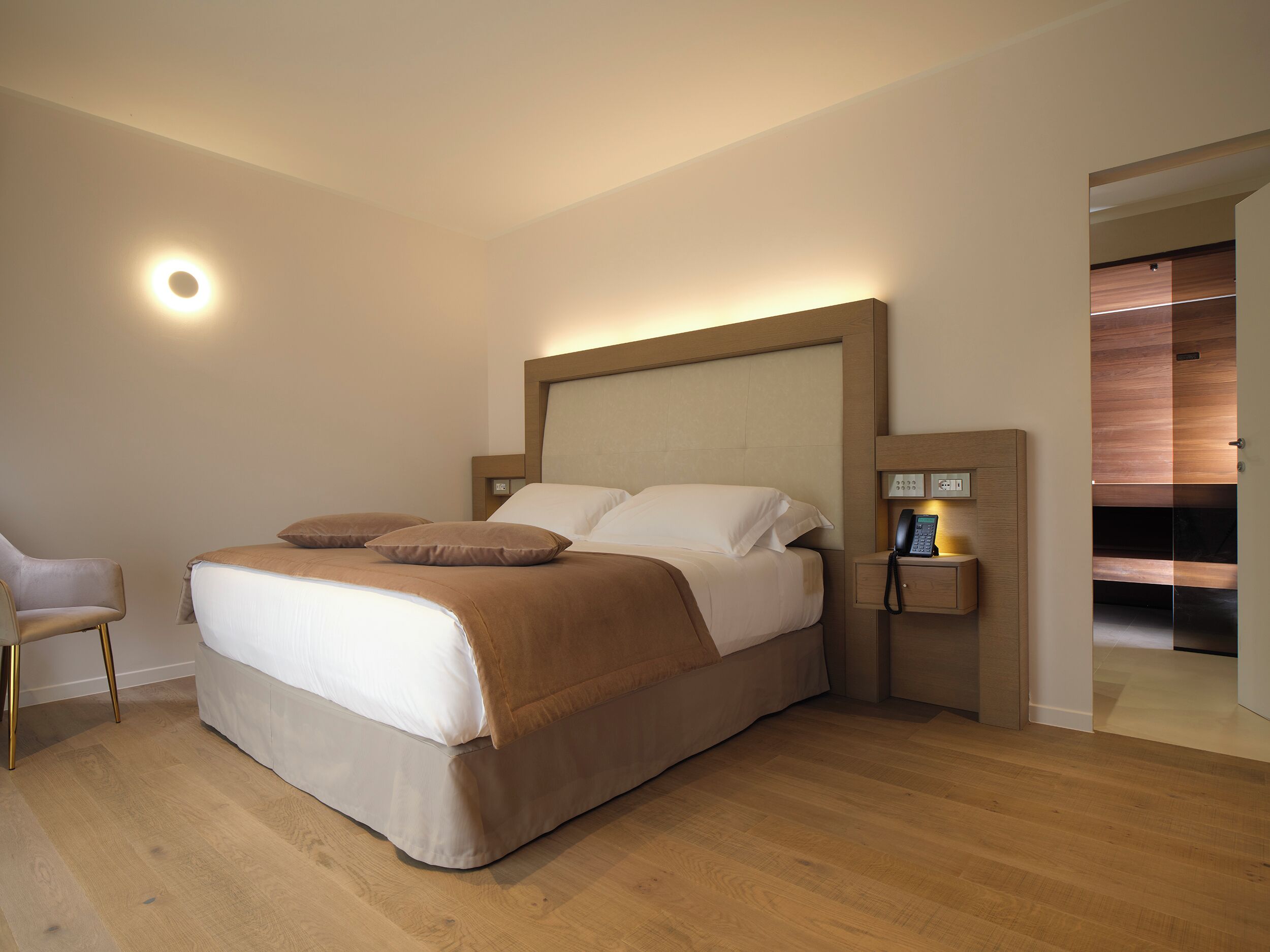 A modern hotel room with a large bed, bedside table, and a chair.