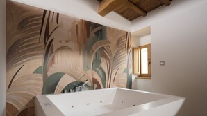 A modern bathroom with a freestanding bathtub, a wooden ceiling beam, and a large wall mural. - Ascesi Resort (Assisi)