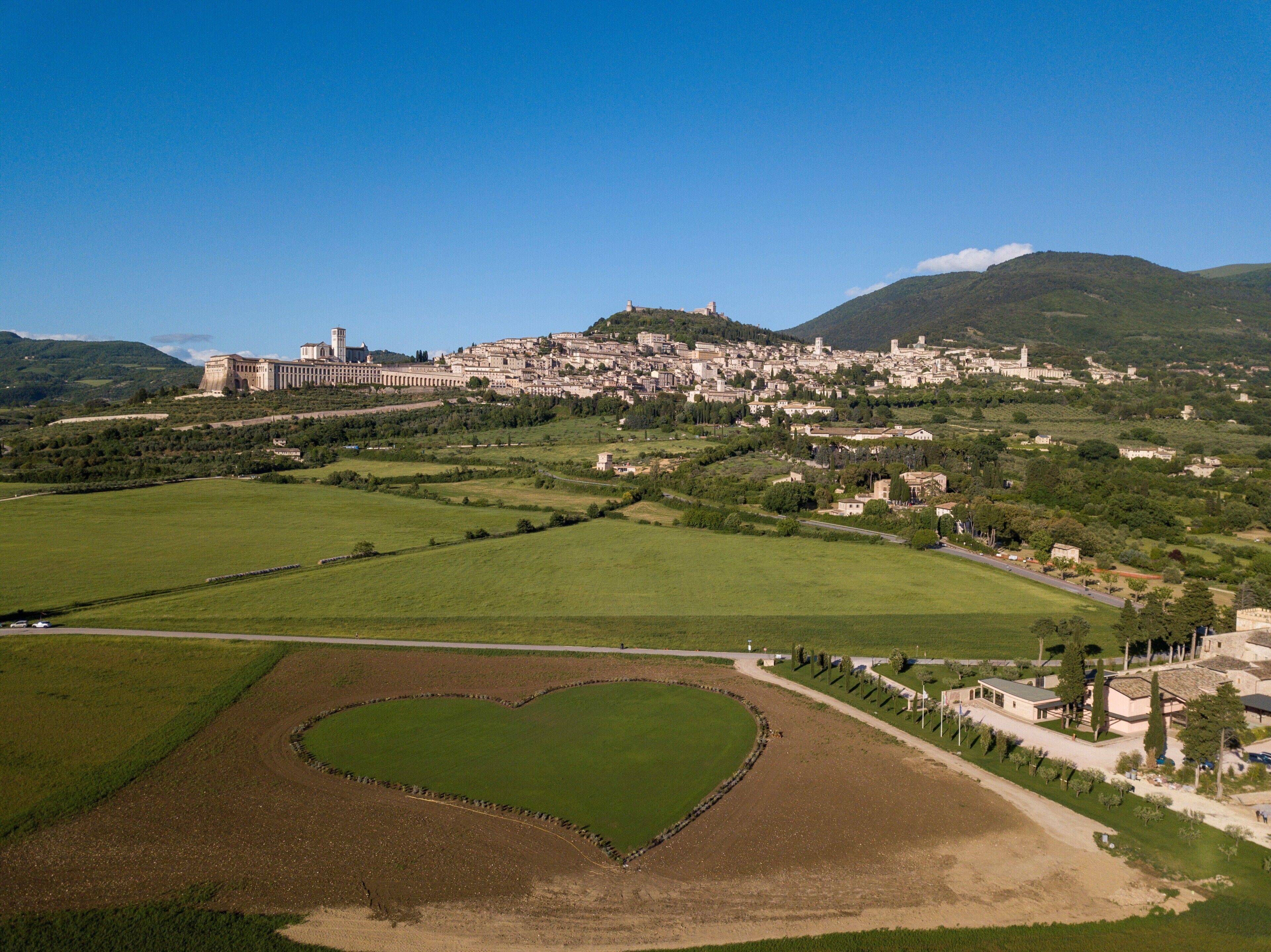 Un gran complexos d'edificis amb diverses estructures, envoltat de camps verds i una zona amb forma de cor.
