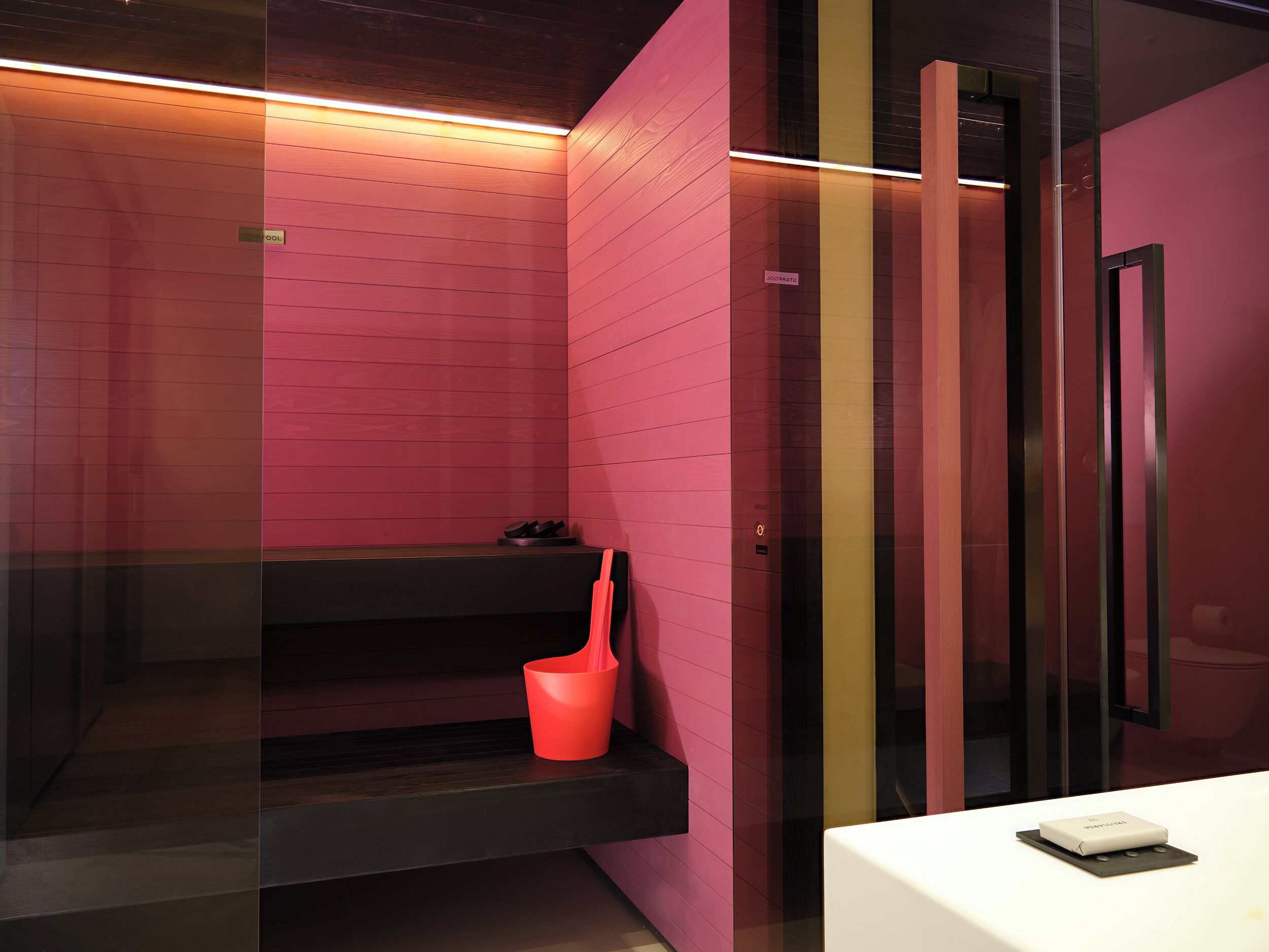 A modern bathroom with pink walls, a black sink, and a red trash bin.