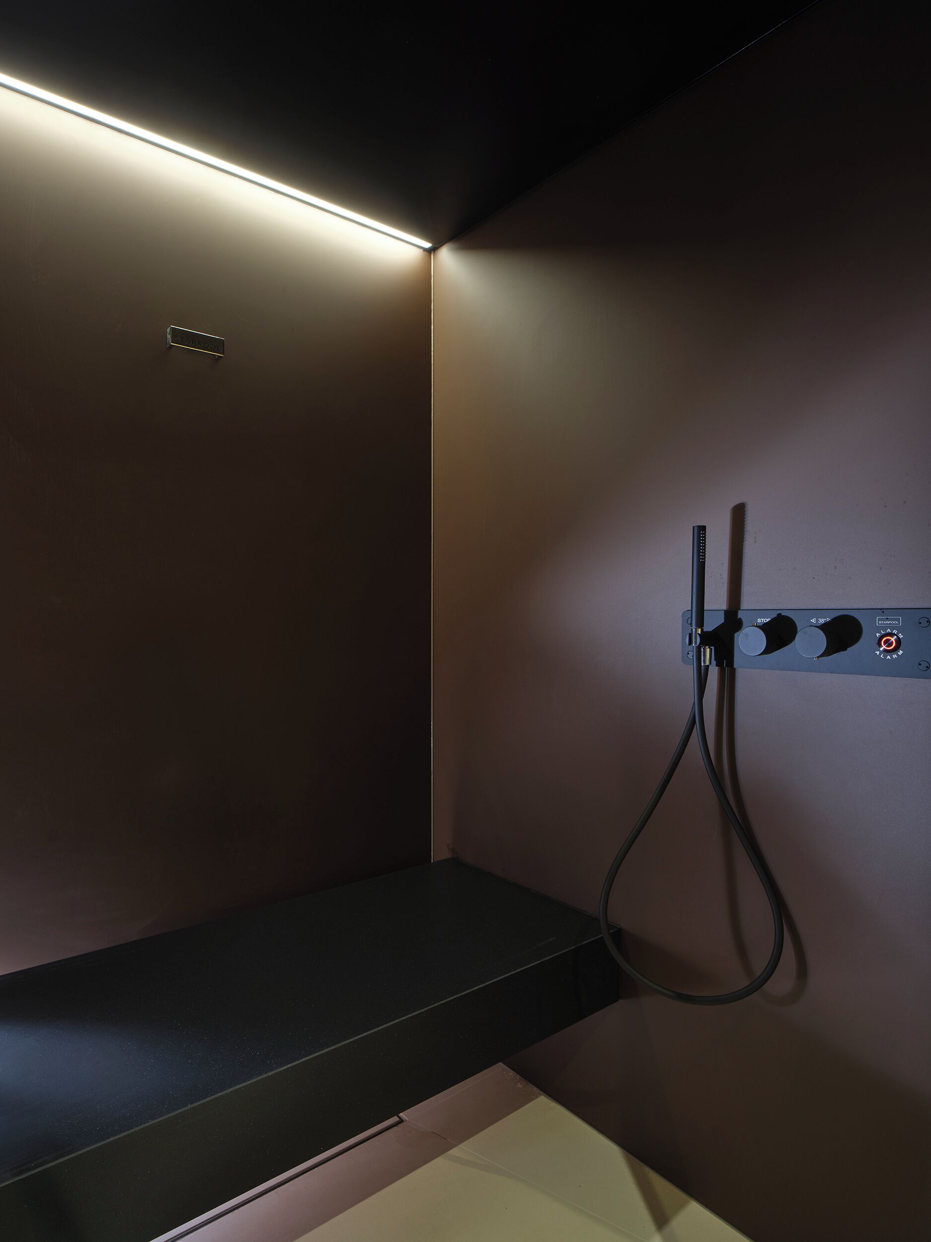 Una habitación con una pared marrón oscuro, un estante negro y un dispositivo fijado a la pared con cables.